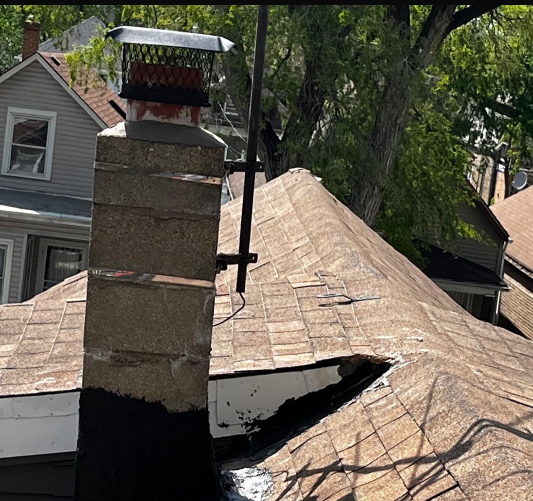 Storm-damaged roof with worn shingles and a leak near the chimney before GRA repair
